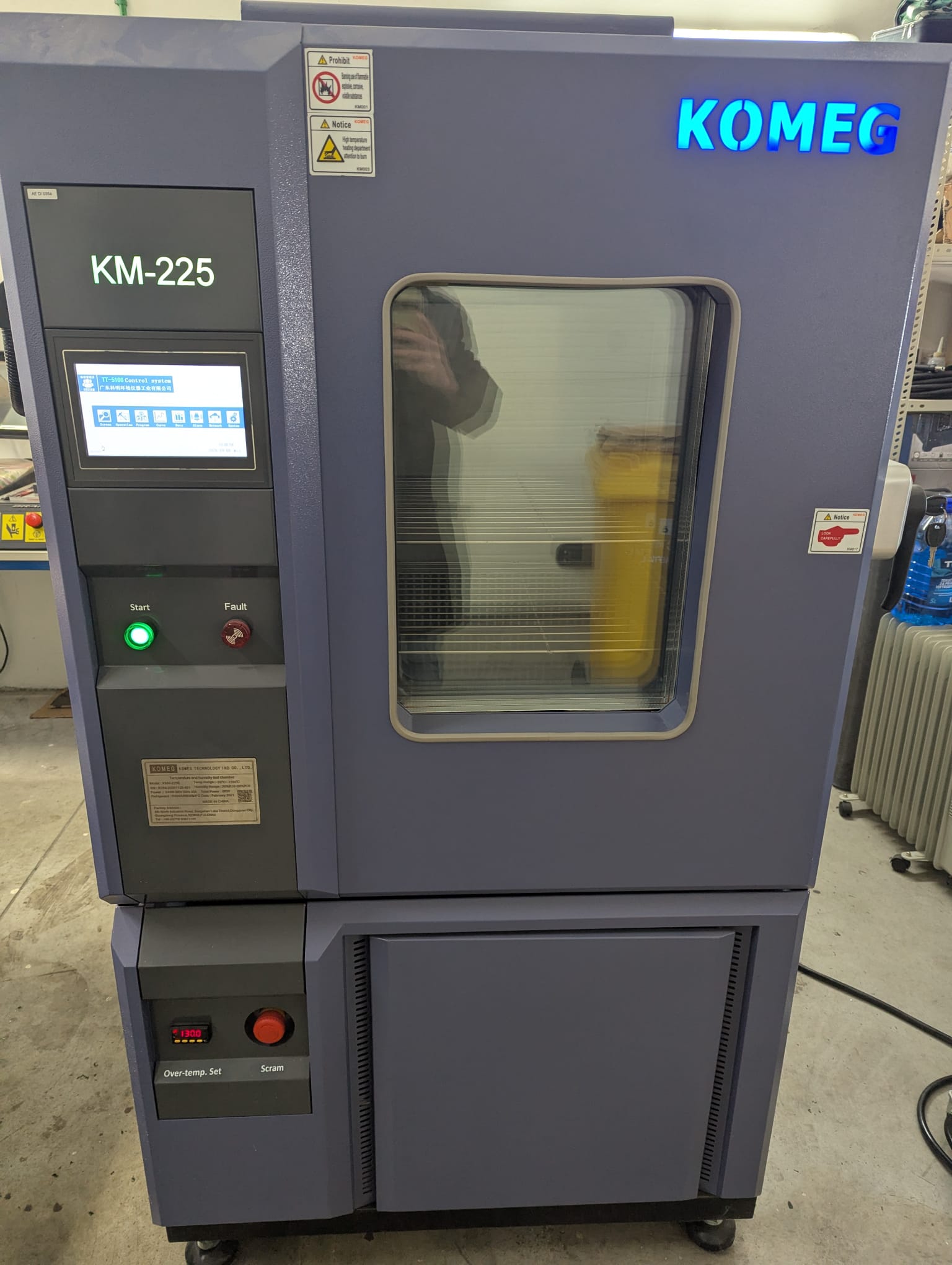 Front view — KOMEG KMH-225L with KM-5166 touchscreen controller, START / FAULT indicators and emergency stop.